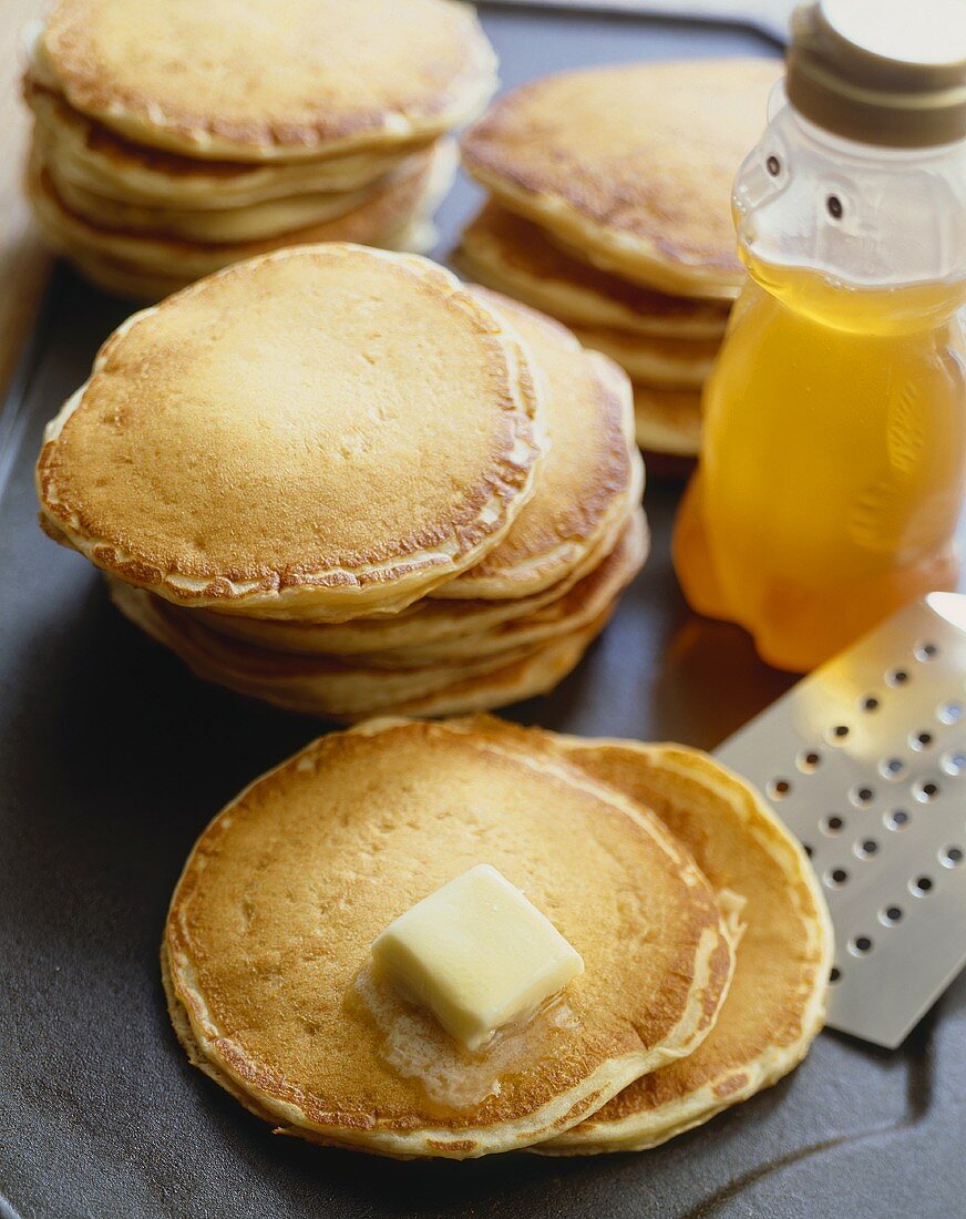 Stacks of Pancakes on a Griddle; Butter Melting on One Stack; Spatula and Honey Bear