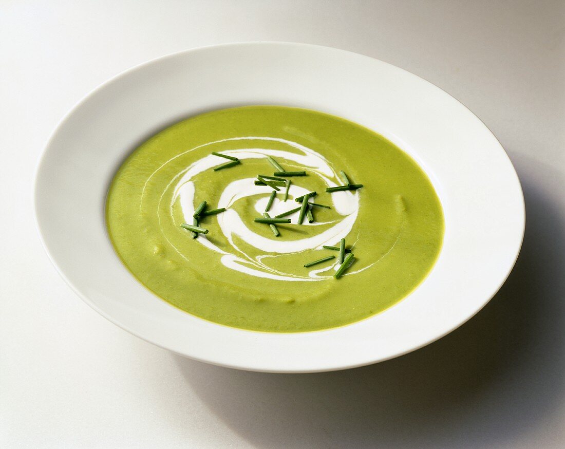 Creamy Pea Soup with Cream Swirl and Chive Garnish in a White Bowl; White Background