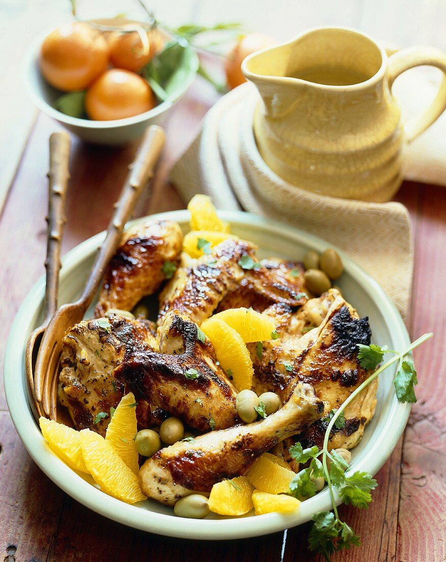 Grilled Chicken with Orange Sections and Green Olives on a Plate; Wooden Fork and Spoon