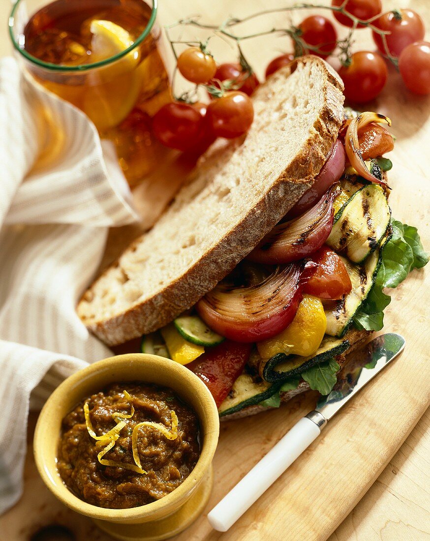 Grilled Vegetable Sandwich on Crusty White Bread; Small Bowl of Vegetable Spread; Tomatoes