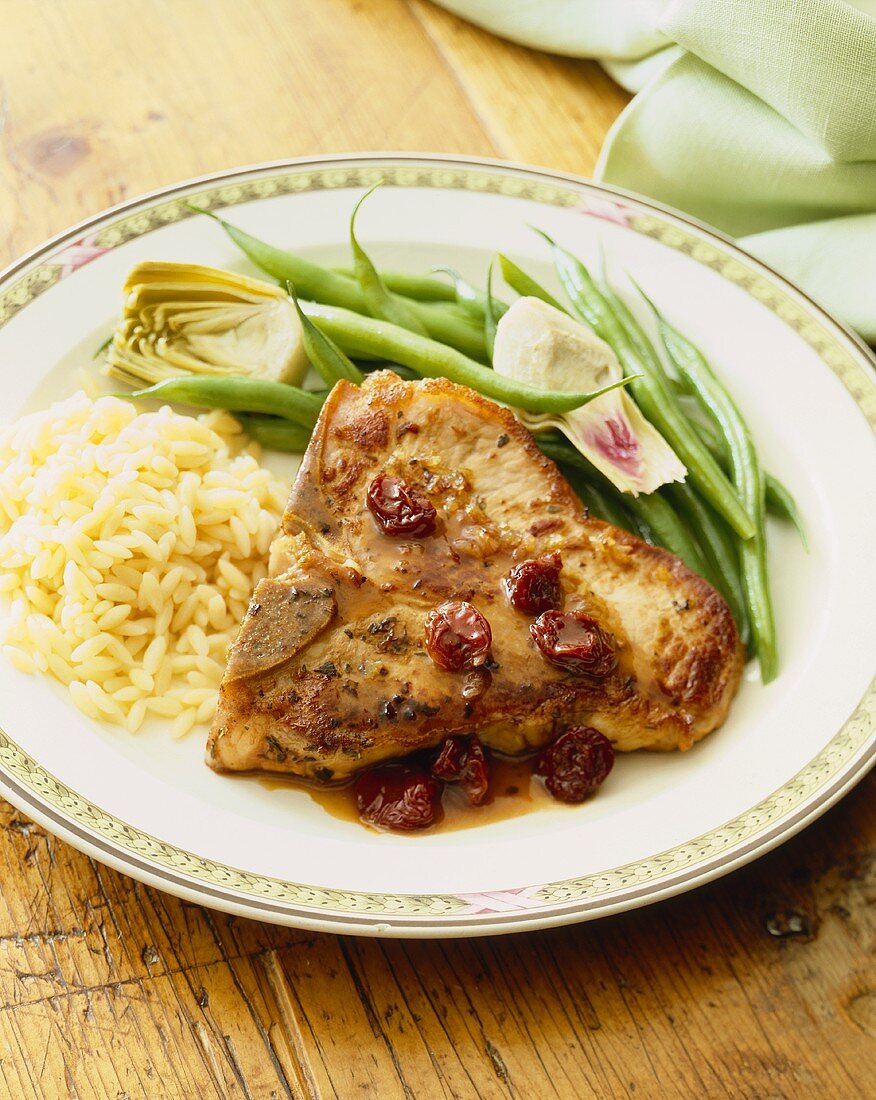 Pork Chop Topped with Dried Cranberry Sauce Served with Rice and Green Beans on a Plate