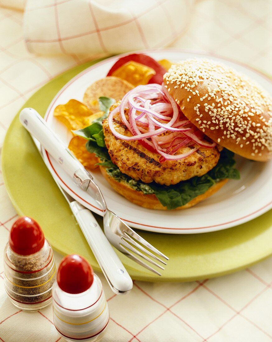 Grilled Turkey Burger with Lettuce and Red Onion on a Sesame Seed Bun on Plate with Chips