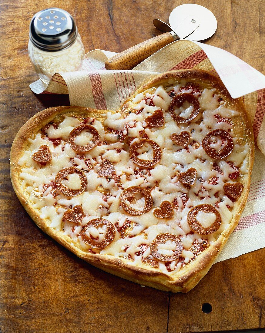 Herzförmige Pizza mit Salamischeiben in Herzform und Käse