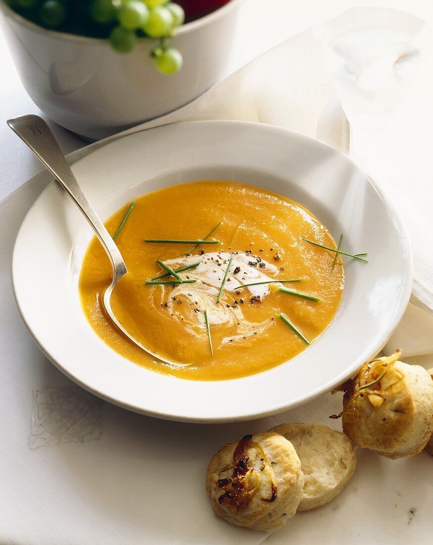 Bowl of Creamy Squash Soup with a Spoon; Biscuits