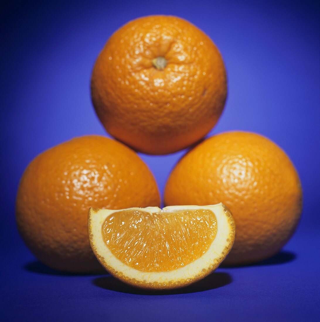 Orangenschnitz vor drei ganzen Orangen
