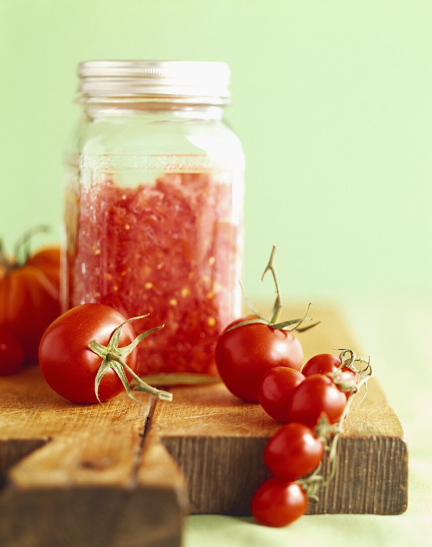 Tomatenpüree im Vorratsglas und frische Tomaten auf Schneidebrett