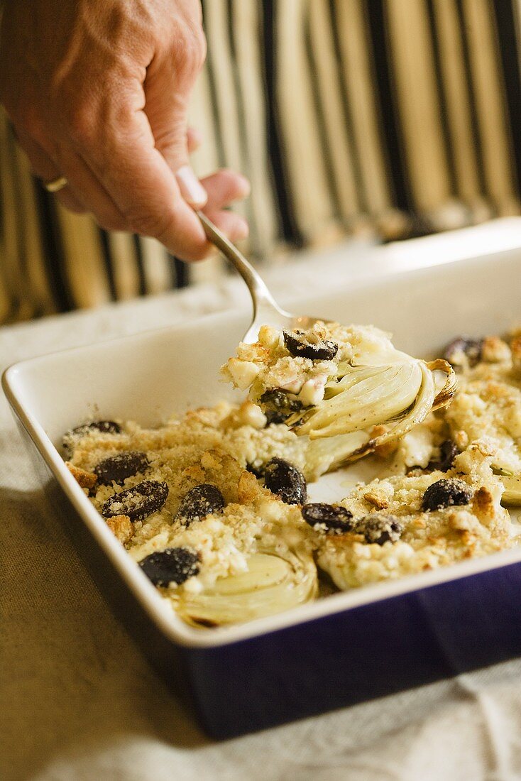 Scooping Baked Fennel with Blue Cheese, Olives and Bread Crumbs from Baking Dish