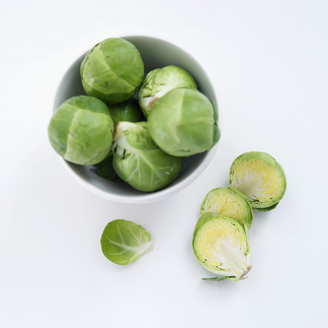 Fresh Brussels Sprouts in and Beside a Bowl; White Background