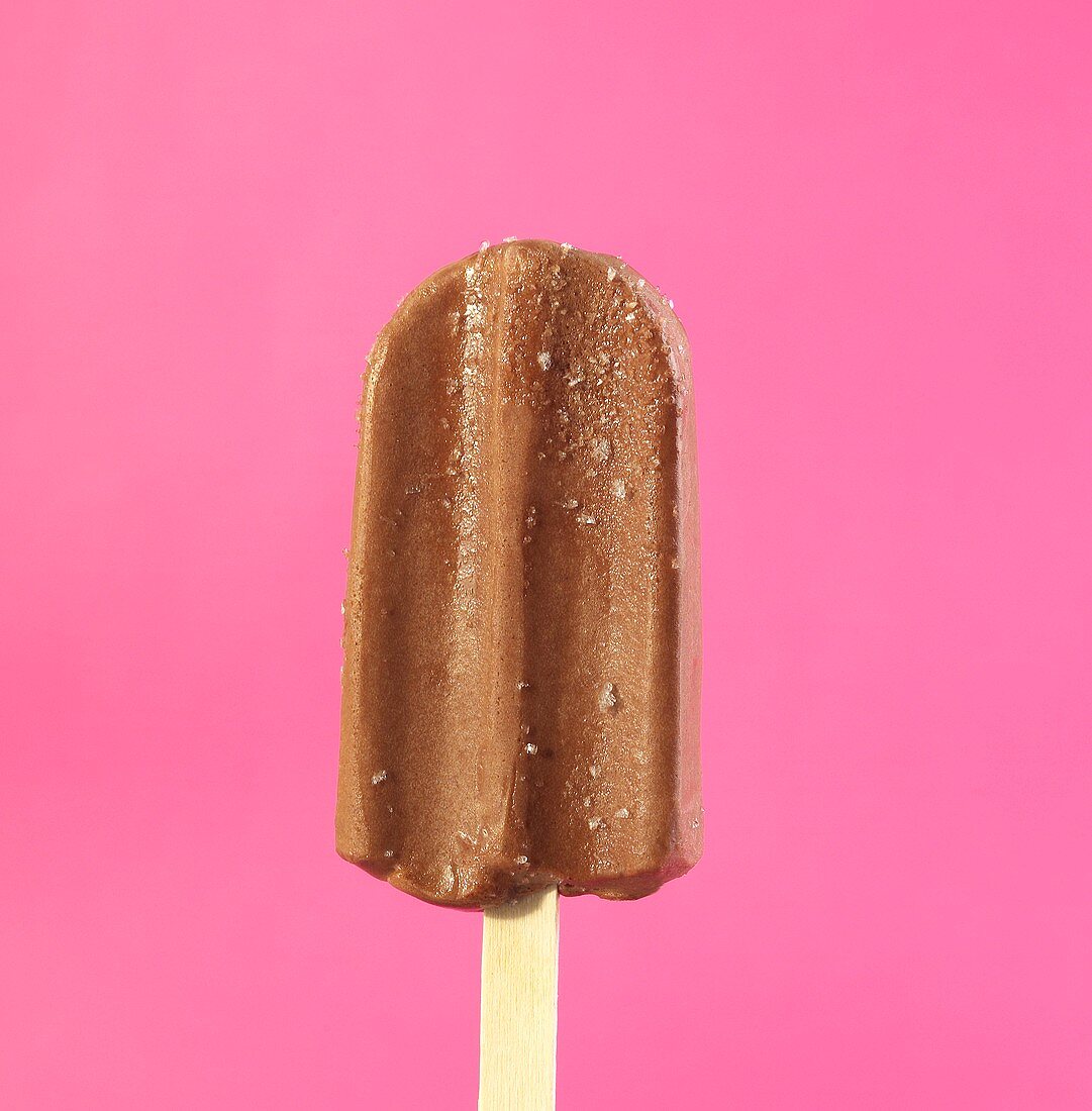 Schokoladen-Eis am Stiel vor rosa Hintergrund