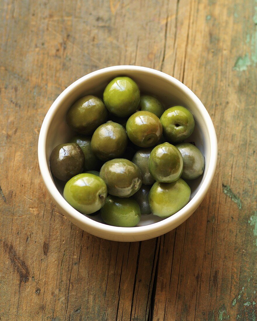Grüne Oliven im Schälchen auf rustikalem Holztisch