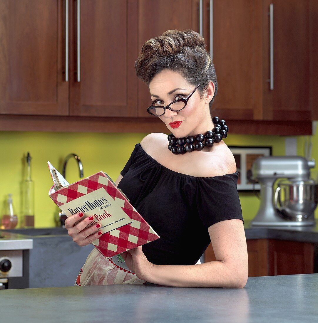 Frau mit Kochbuch im Stil der 50er Jahre in der Küche