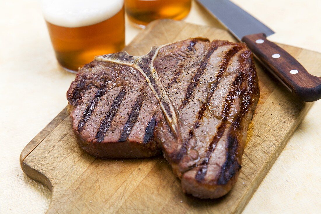 Grilled T-Bone Steak on Cutting Board; Knife and Beer