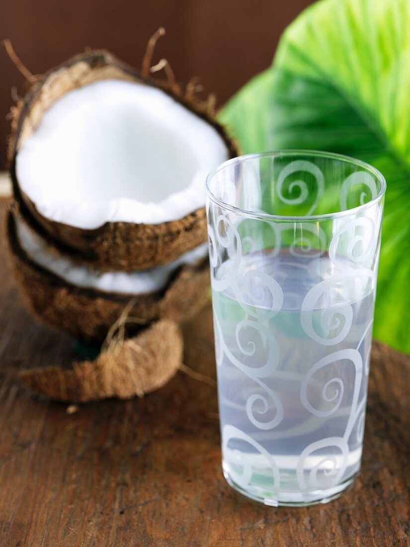 Glas Kokoswasser vor aufgeschlagener Kokosnuss