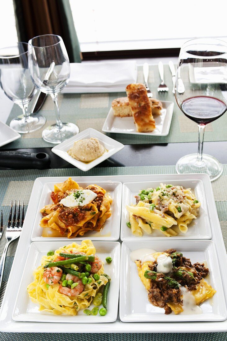 Four Assorted Pasta Dishes on Four Square White Plates; With Wine