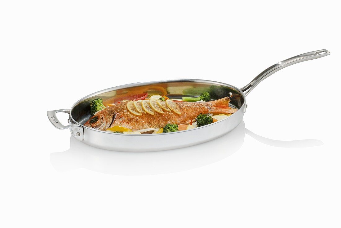 Whole Cooked Fish in a Skillet with Lemon Slices and Broccoli