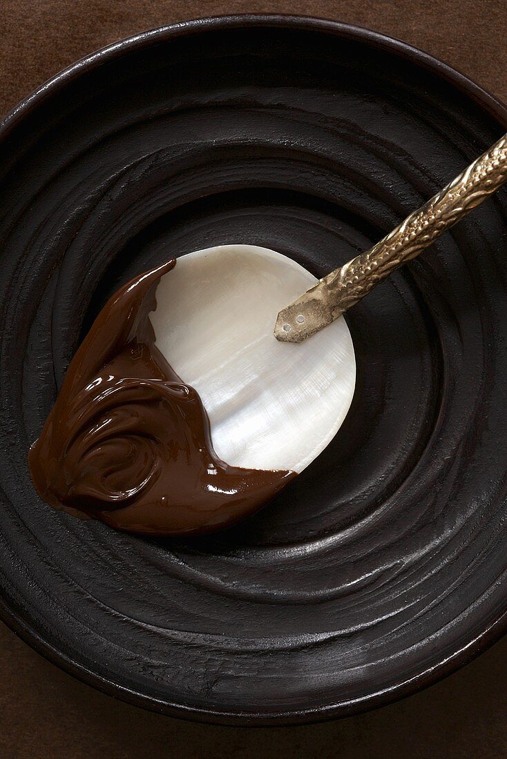 Geschmolzene Schokolade auf Permuttlöffel in schwarzer Schale