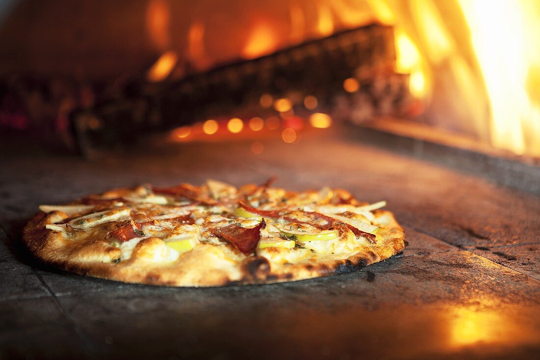 Pizza mit Äpfeln & Prosciutto, im Hintergrund Ofenfeuer