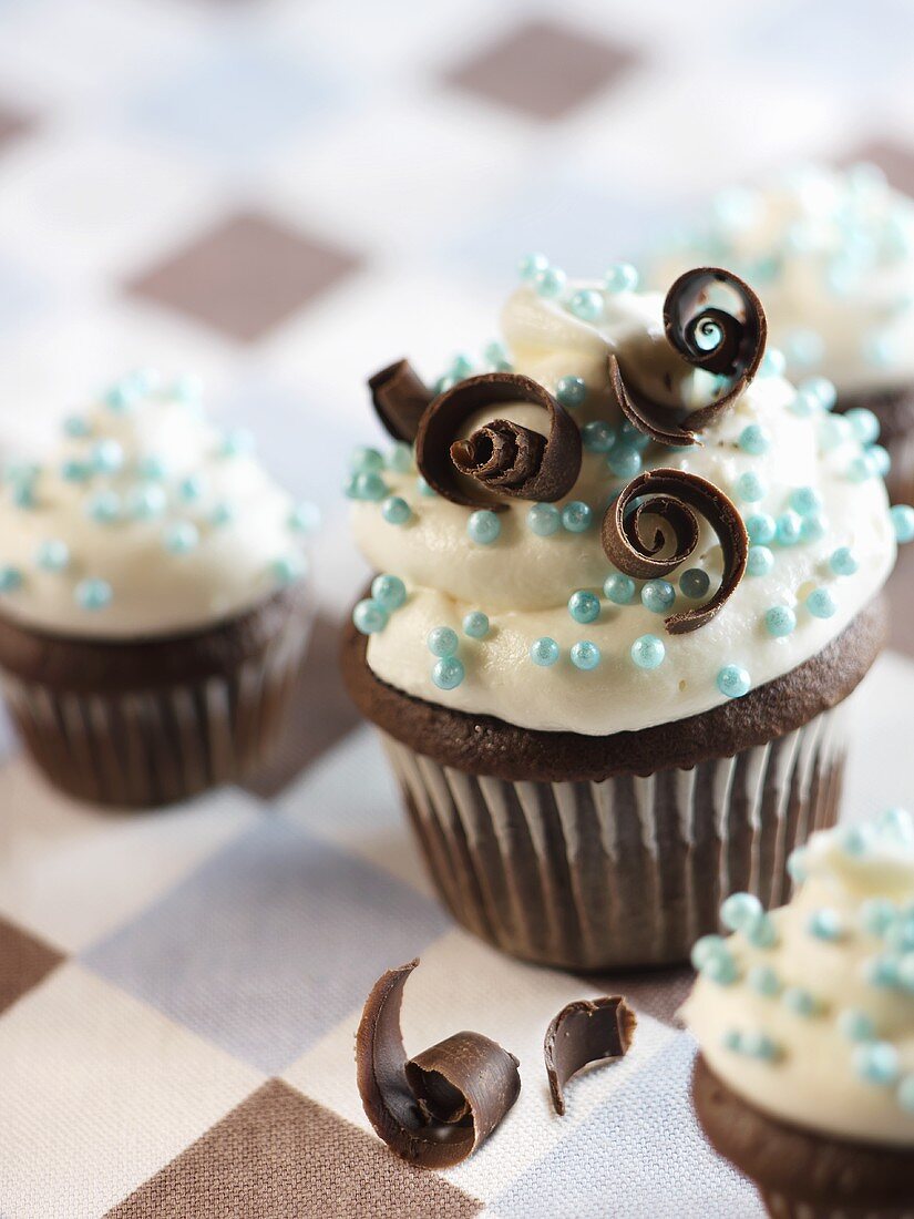 Schokoladencupcakes mit Vanilleglasur, blauen Zuckerperlen und Schokoröllchen