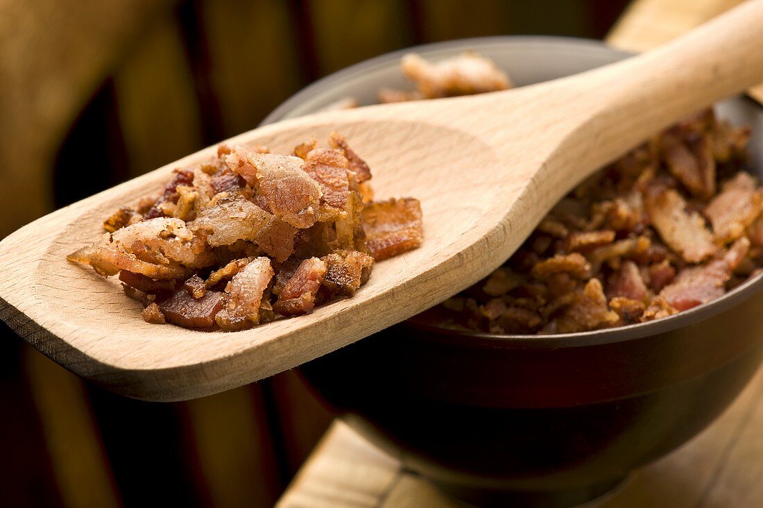 Knusprige Bacon Bits (Speckwürfel) in Holzschale und auf Kochlöffel