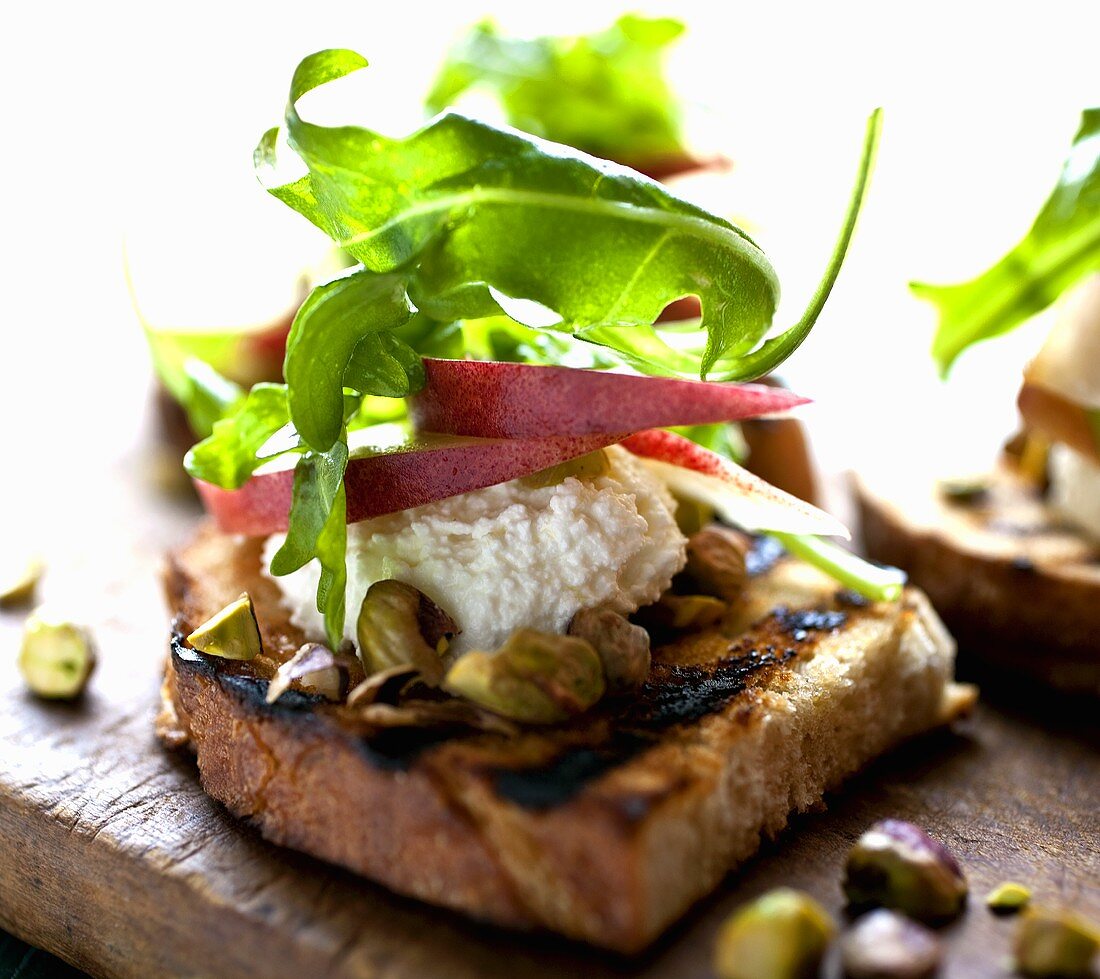 Crostini Topped with Cheese, Pear Slices, Pistachios and Arugula