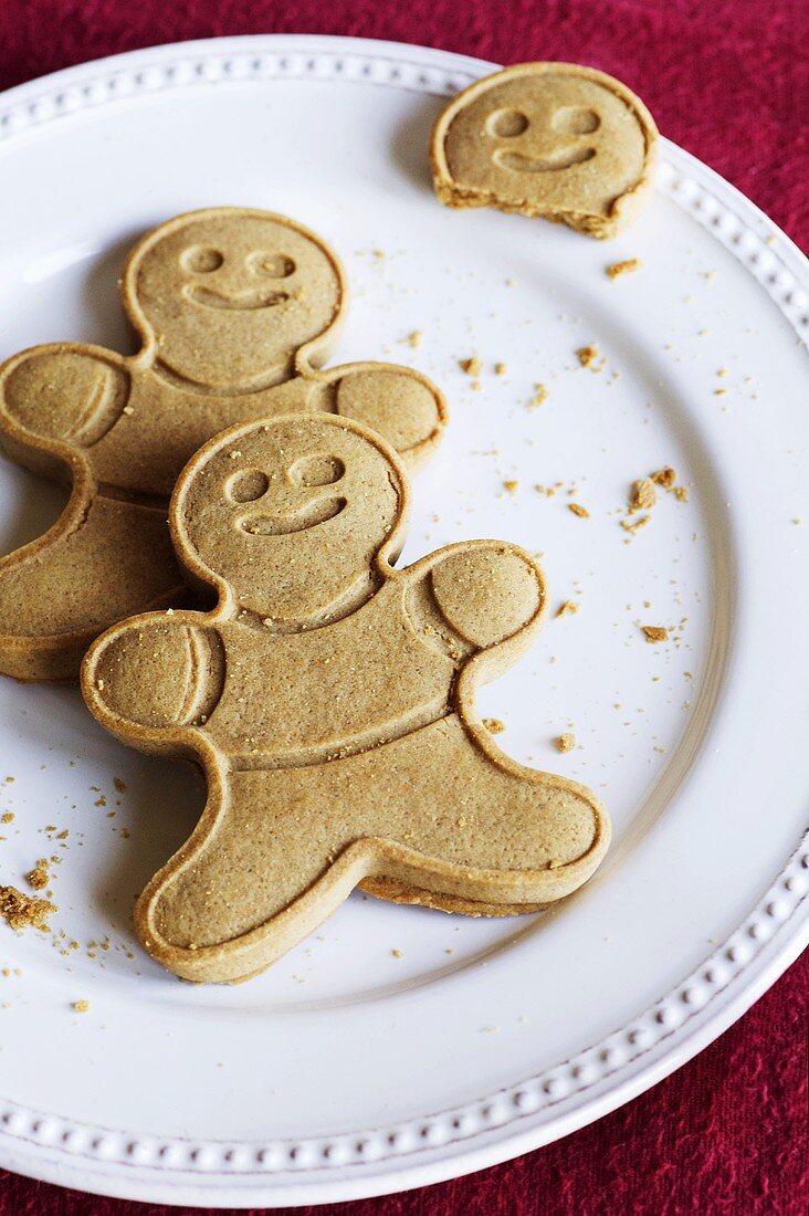 Two Whole Gingerbread Men and One Gingerbread Man Head; On a White Plate