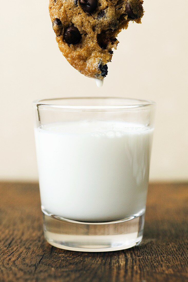 Chocolate Chip Cookie with Bites Taken Out Dipping into a Glass of Milk
