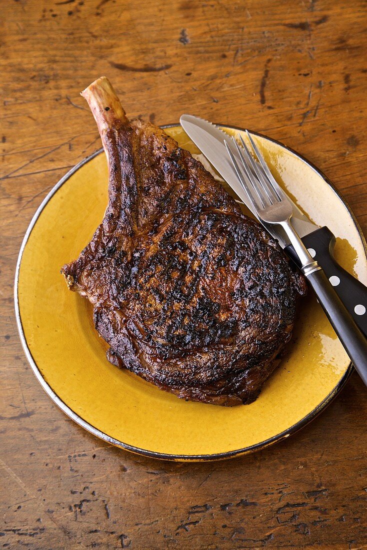 Grilled Steak on a Yellow Plate; Knife and Fork