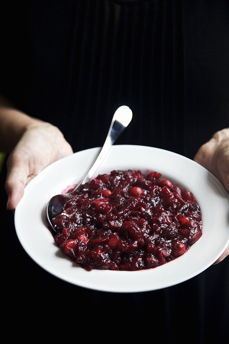 Hände halten Teller mit Cranberrysauce