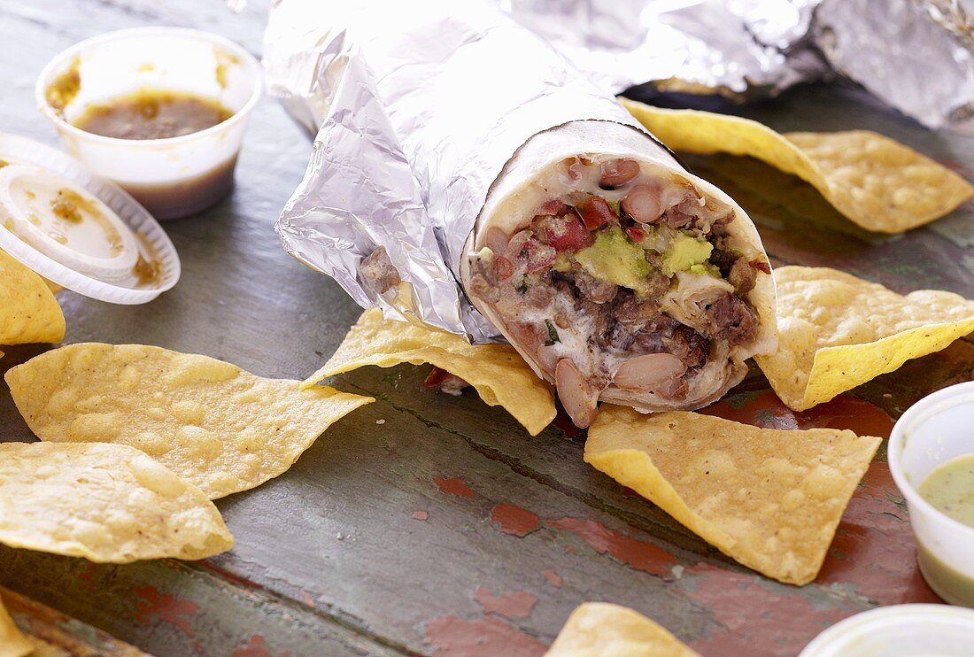 Grosser Burrito, mit Folie umwickelt, mit Tortillachips und Salsa