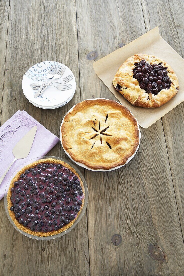 Three Pies on a Wooden Table; Blueberry, Plum and Cherry; Plates and Forks