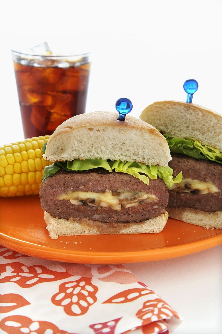 Cheese Stuffed Hamburger; Halved on a Plate with Corn on the Cob; Glass of Coke
