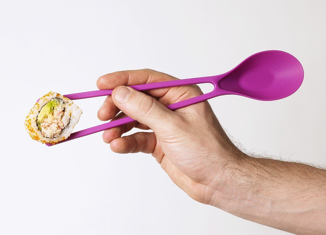 Männliche Hand hält Sushi zwischen Stäbchen