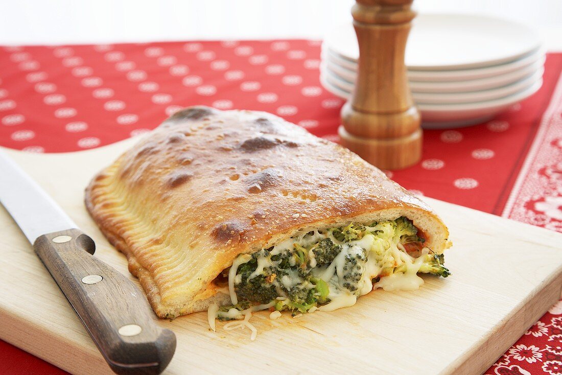 Broccoli and Cheese Calzone with End Cut Off; On Cutting Board with Knife