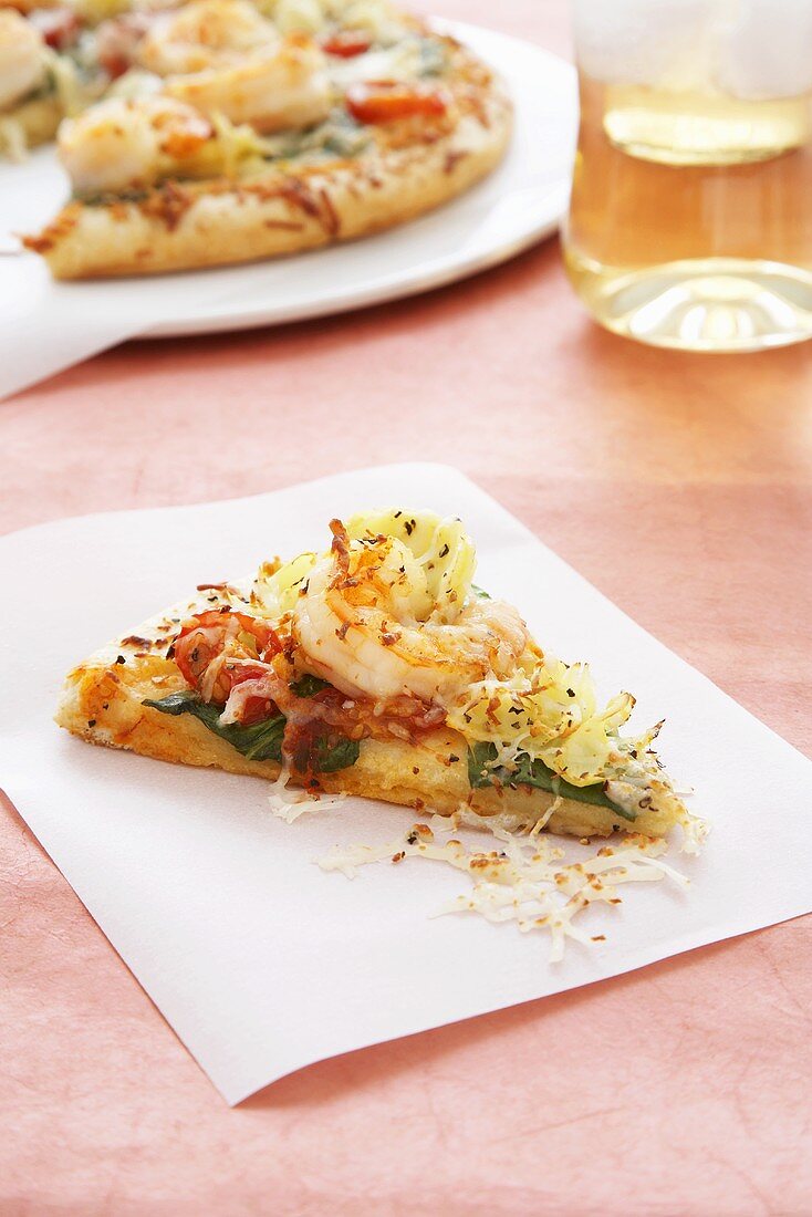 Ein Stück Pizza mit Shrimps vor angeschnittener Pizza
