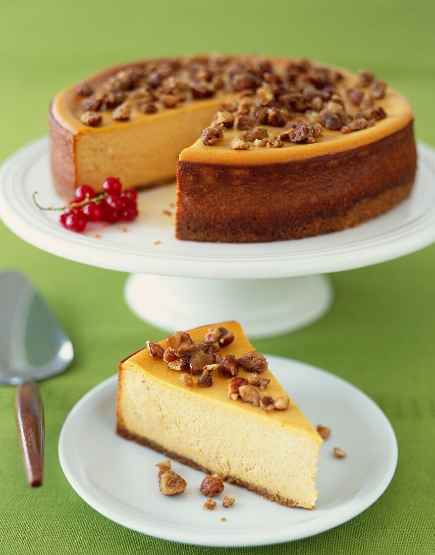 Slice of Pumpkin Cheesecake with Nut Topping; Whole Cheesecake with Slice Removed in Background