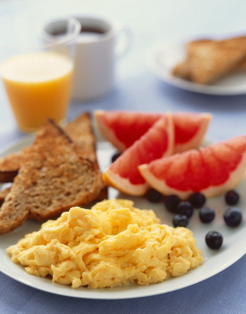 Frühstücksteller mit Rührei, Vollkorntoast, Obst und Orangensaft