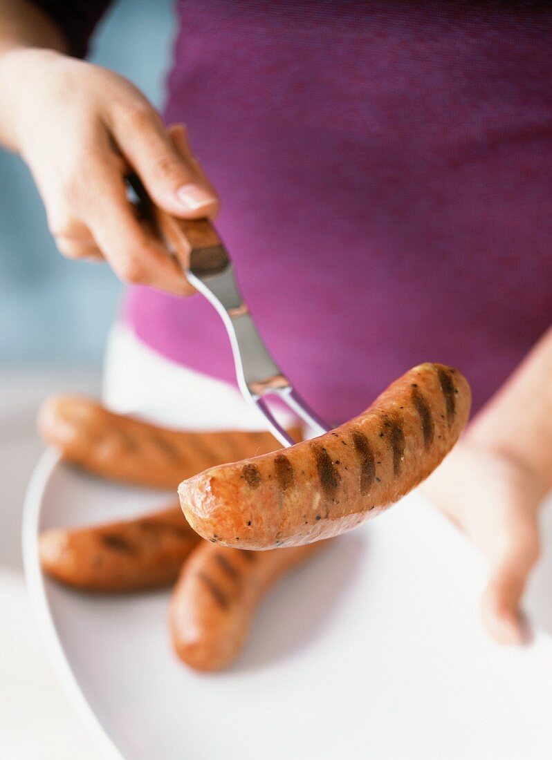 Frau hält Fleischgabel mit aufgespiesster Bratwurst