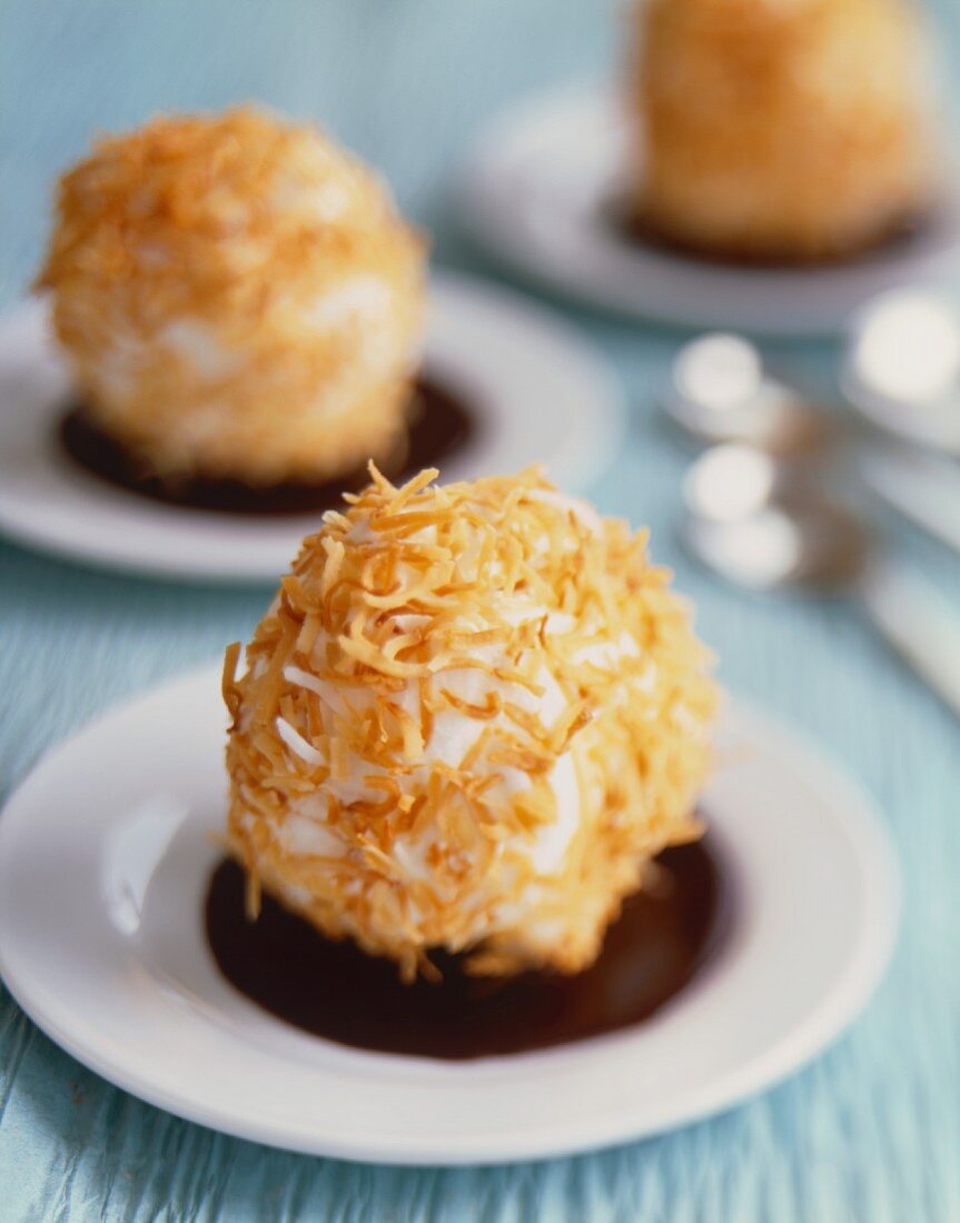 Scoops of Sorbet Rolled in Toasted Coconut Sitting in Chocolate Sauce