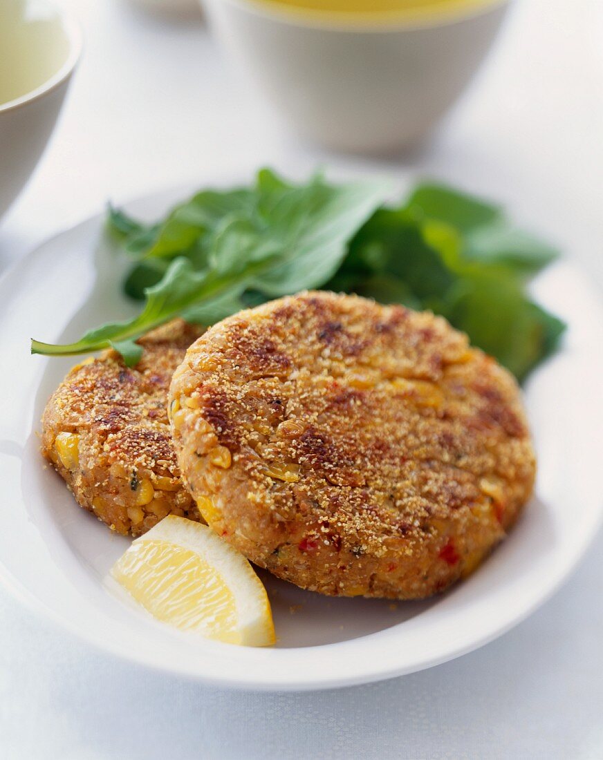 Two Corn and Chickpea Patties on a Plate with Lemon and Greens