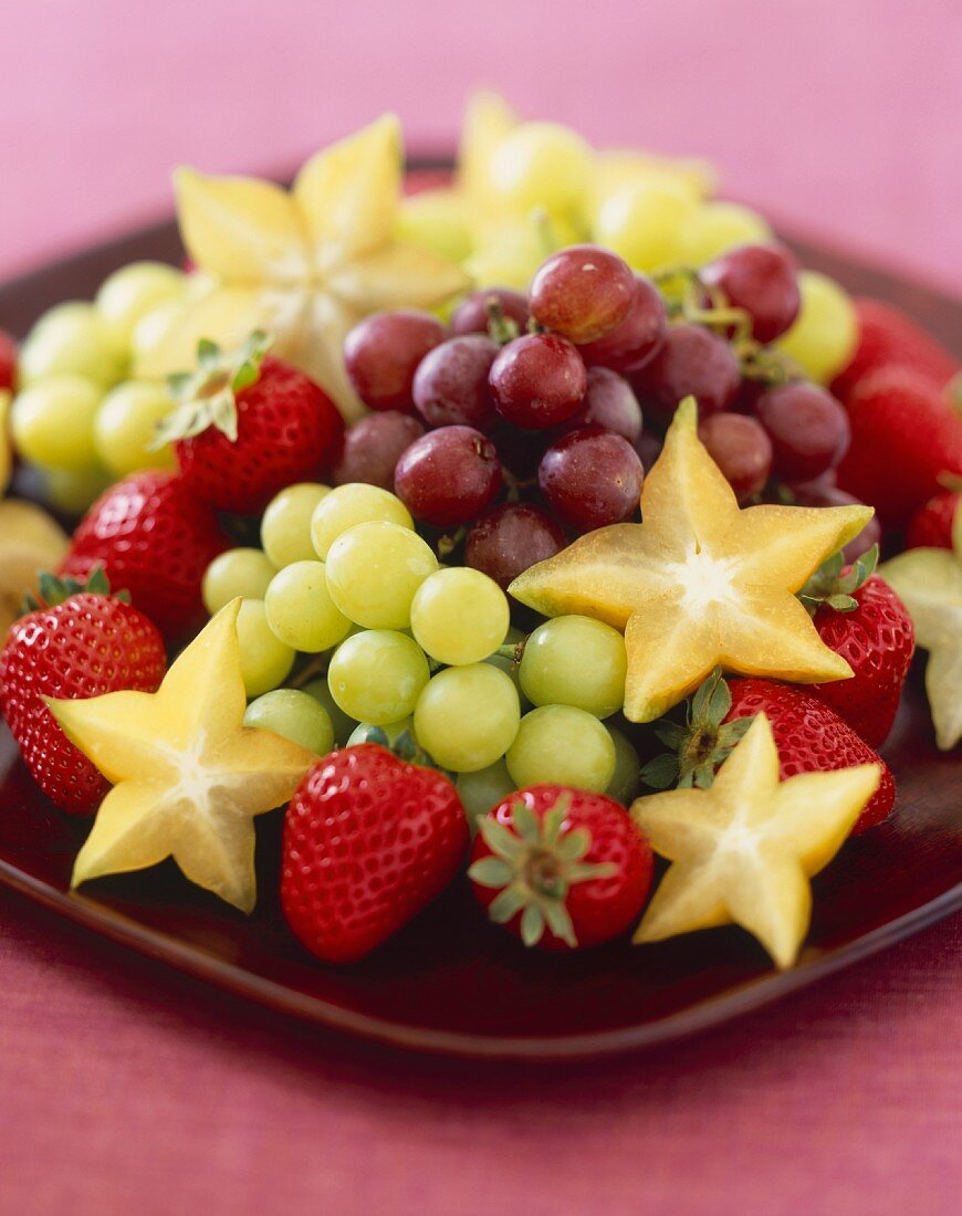Obstteller mit roten und grünen Trauben, Karambolen und Erdbeeren