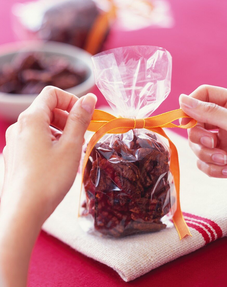 Hands Tying a Ribbon onto a Gift Bag of Candied Pecans