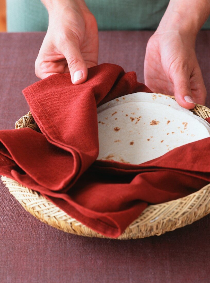 Hände halten Korb mit erwärmten Tortillas in einer Serviette