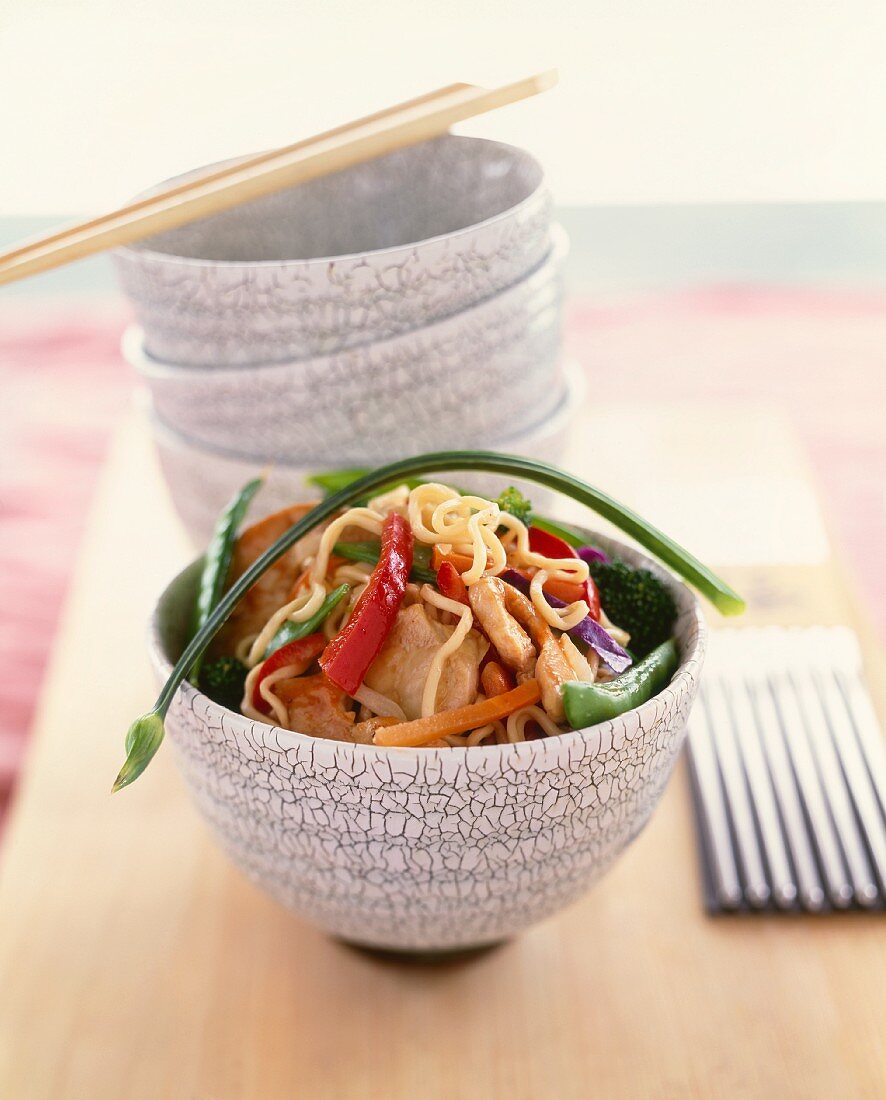 Asian Noodles with Chicken and Vegetables in a Bowl; Stacked Bowls and Chopsticks in the Background