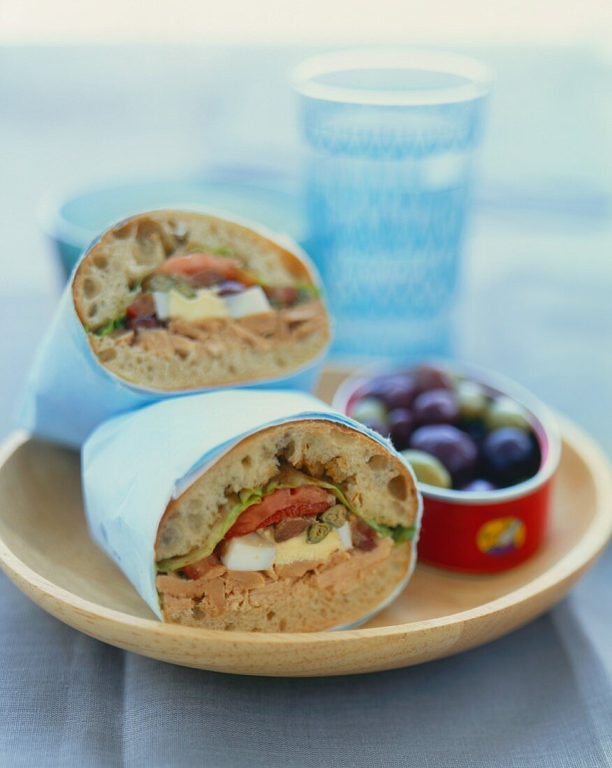 Tuna, Anchovy, Caper and Egg Sandwich; Wrapped in Paper; Bowl of Olives