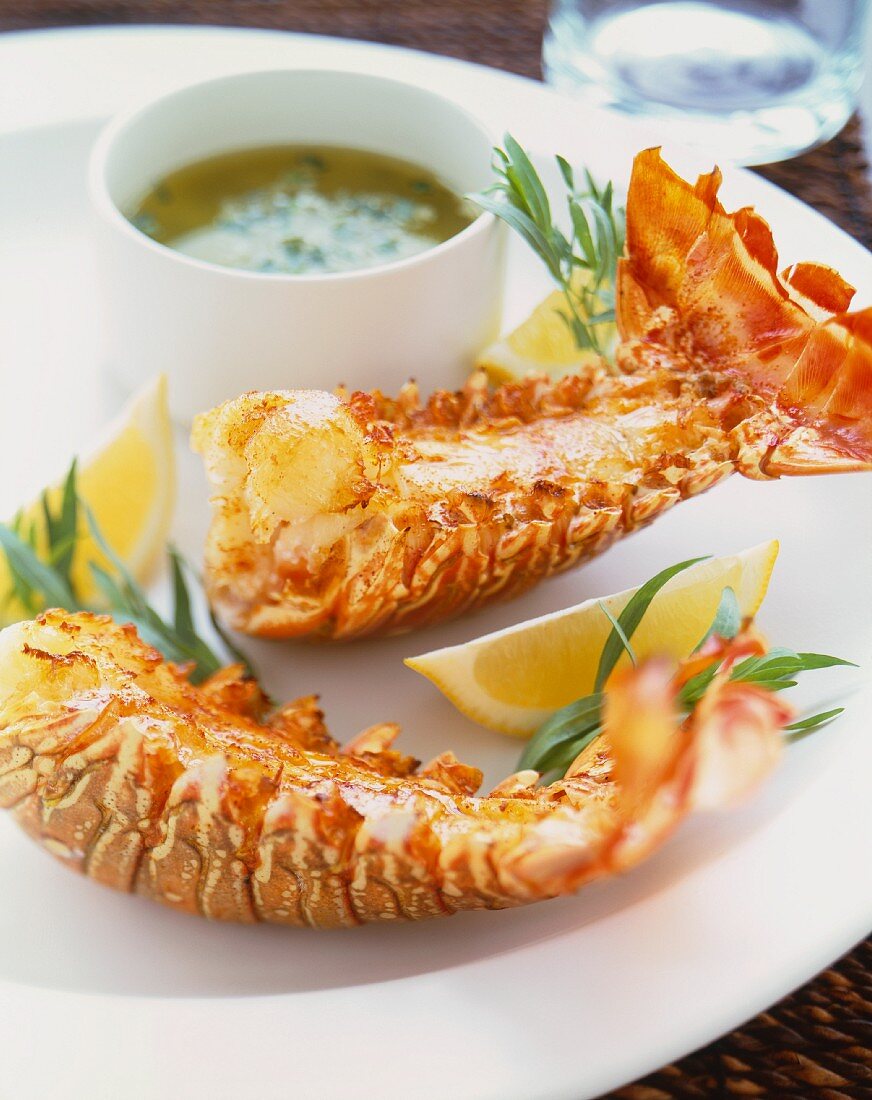 Two Lobster Tails on a White Plate with Lemon Wedges and Dipping Sauce