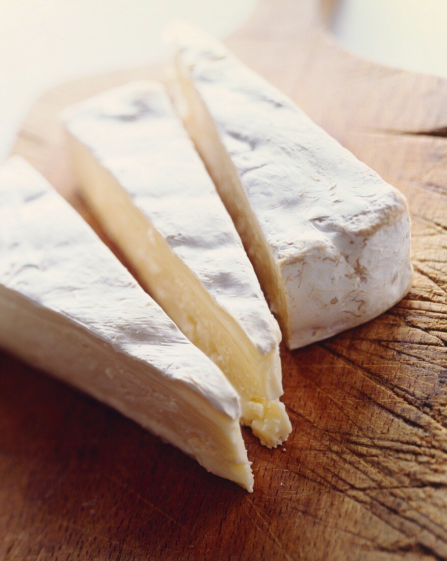 Three Wedges of Brie Cheese on a Cutting Board