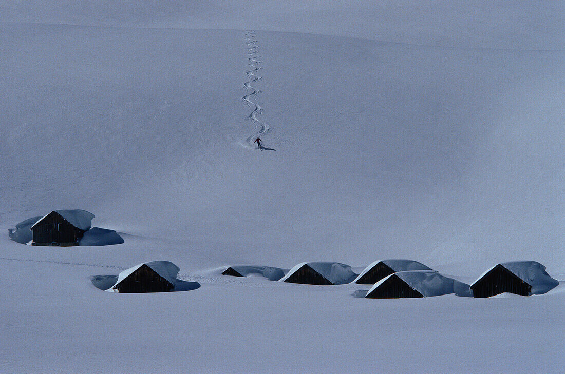 Skier and snow-covered cabins, Alps, Europe