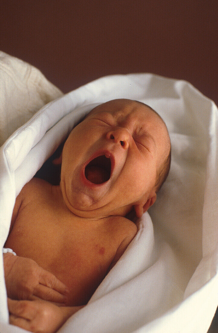 Newborn baby yawns, wrapped in blanket, Germany