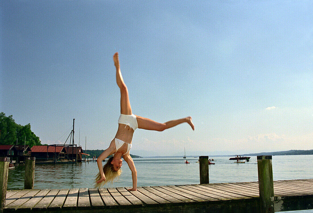 Young woman do handstand on jetty, Starnberger See, Bavaria, Germany