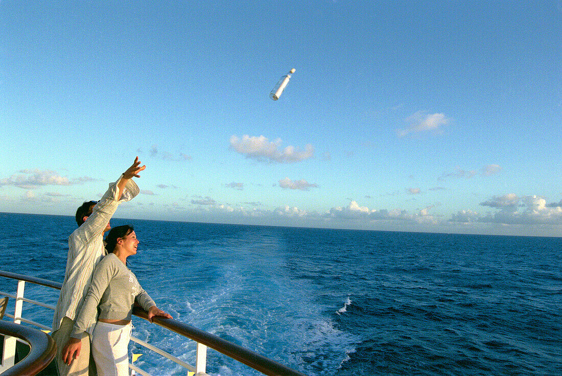 Young couple throwing message in a bottle into the sea, Cruise ship Aida, Caribbean, America